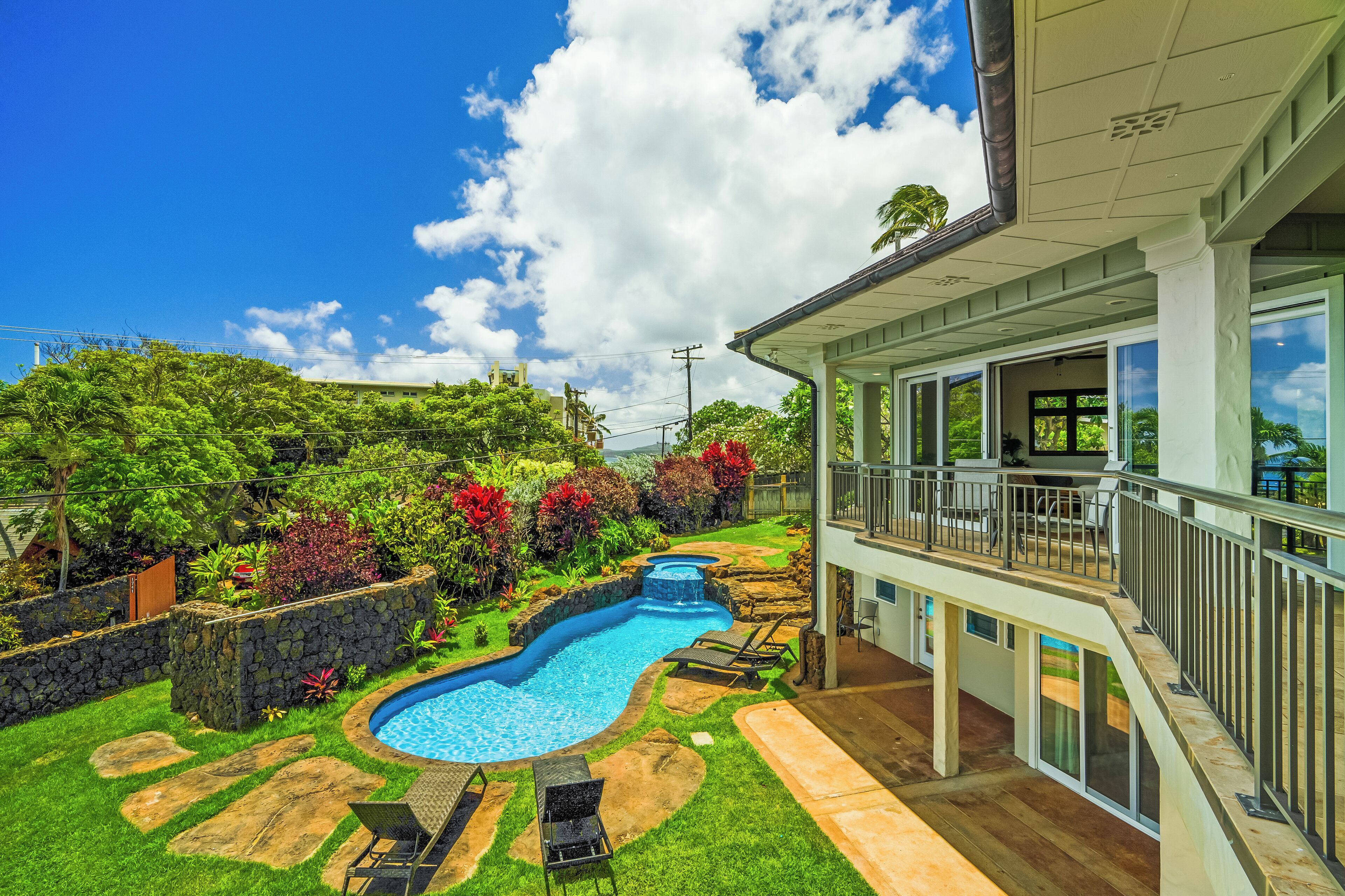 A swimming pool with a waterfall feature, surrounded by a stone wall and lush greenery.