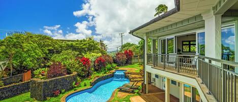 A swimming pool with a waterfall feature, surrounded by a stone wall and lush greenery.