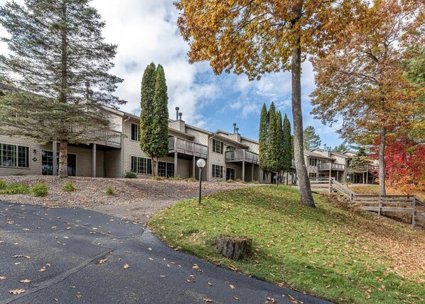 A building with a covered walkway, a grassy area, and trees with autumn leaves.