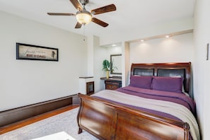 A bedroom with a wooden bed, a ceiling fan, a framed inspirational quote, and a small bedside table with a plant.