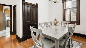 A dining room with a wooden table, grey chairs, a chandelier, and a window with shutters. - The Shipoke Brickhouse (Harrisburg)