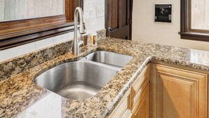 A kitchen with granite countertops, a stainless steel sink, wooden cabinets, and a window with a view of a fence and buildings. - The Shipoke Brickhouse (Harrisburg)