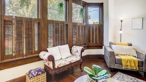 A room with a corner sofa, a grey armchair, a floor lamp, and a large window with wooden shutters. - The Shipoke Brickhouse (Harrisburg)