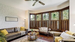 A living room with a sofa, armchairs, a coffee table, and a large window with shutters. - The Shipoke Brickhouse (Harrisburg)