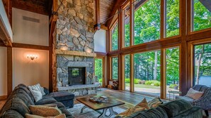 A spacious living room with a stone fireplace, large windows, and a cozy seating area. - Magnificent 7bdrm 8bath luxury on Lake Joe! Hot Tub! Gym! Boathouse! Sauna! (Seguin)