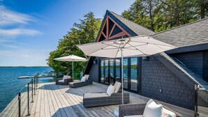A modern outdoor deck with wicker furniture and umbrellas, overlooking a body of water. - Magnificent 7bdrm 8bath luxury on Lake Joe! Hot Tub! Gym! Boathouse! Sauna! (Seguin)
