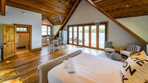 A spacious bedroom with a large bed, a view of the outdoors through a sliding door, and a kitchen area with a dining table and chairs. - Magnificent 7bdrm 8bath luxury on Lake Joe! Hot Tub! Gym! Boathouse! Sauna! (Seguin)
