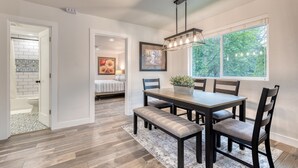 A dining area with a wooden table, benches, and chairs. There is a window with a view of trees and a ceiling light fixture. - 1905 Farmhouse w/ Fresh Make Over ☼ 3 BR / 2 BA (Mountlake Terrace)
