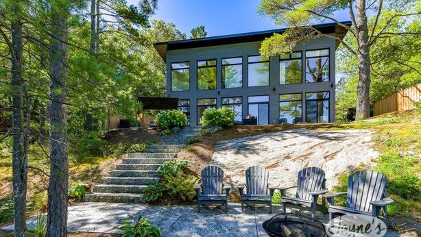 A modern house with a large glass facade, surrounded by trees and a stone staircase leading to the entrance.