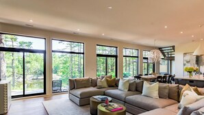A spacious living room with a large sectional sofa, a fireplace, and a view of a forest through large windows.