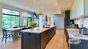 A modern kitchen with a central island, pendant lights, and a view of the outdoors.