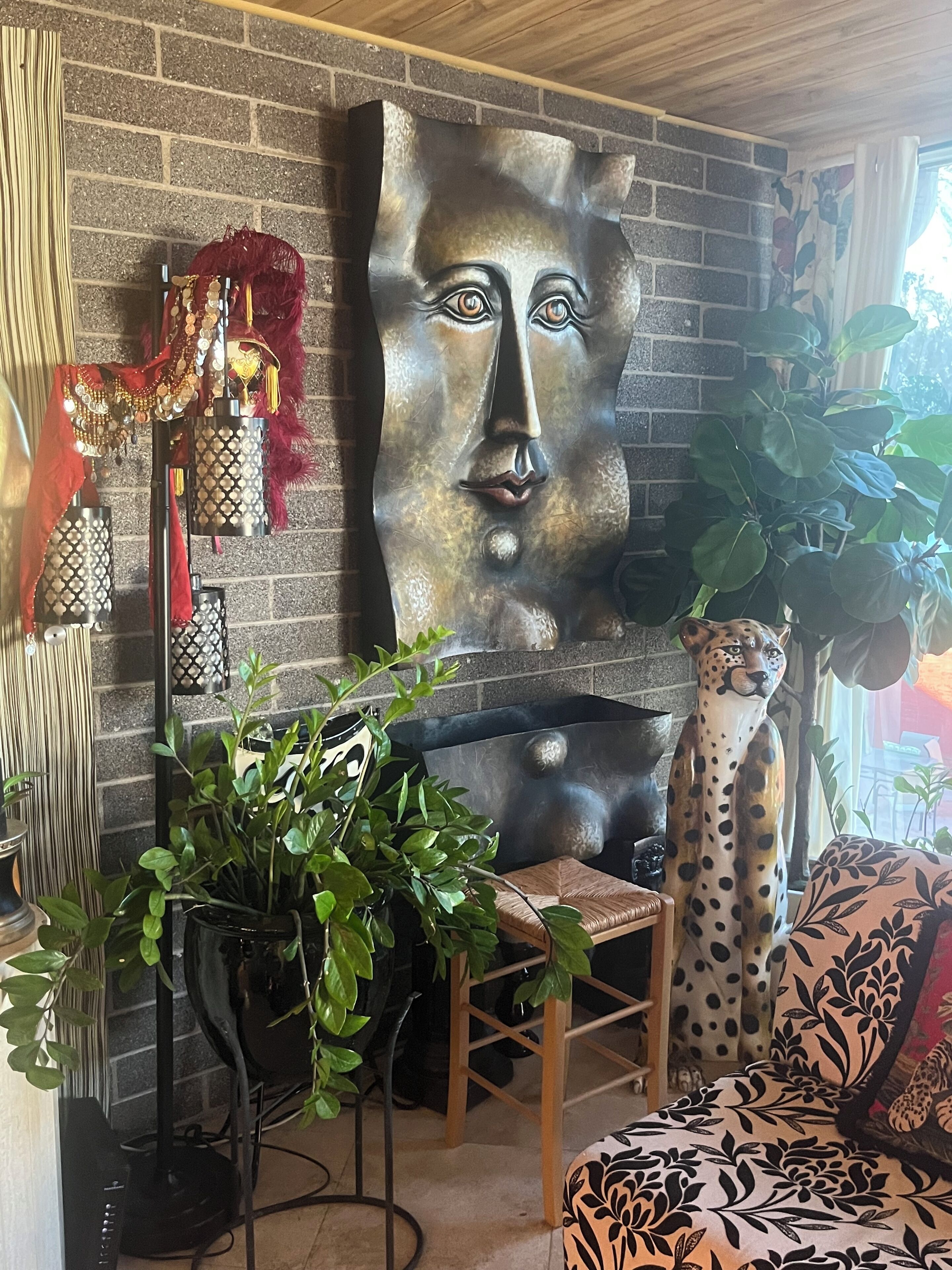 A modern living room with a brick wall, a large abstract metal sculpture, a leopard statue, and a variety of plants.