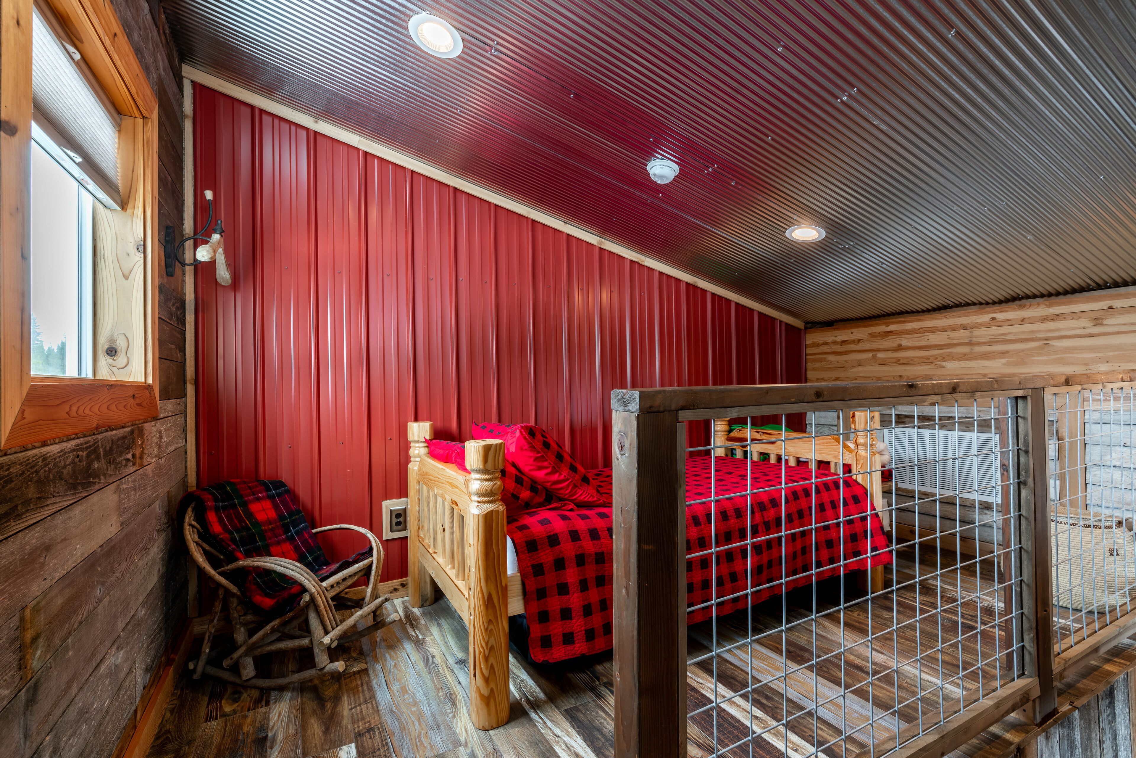 A cozy cabin room with a wooden rocking chair, a bed with red bedding, and a metal cage.