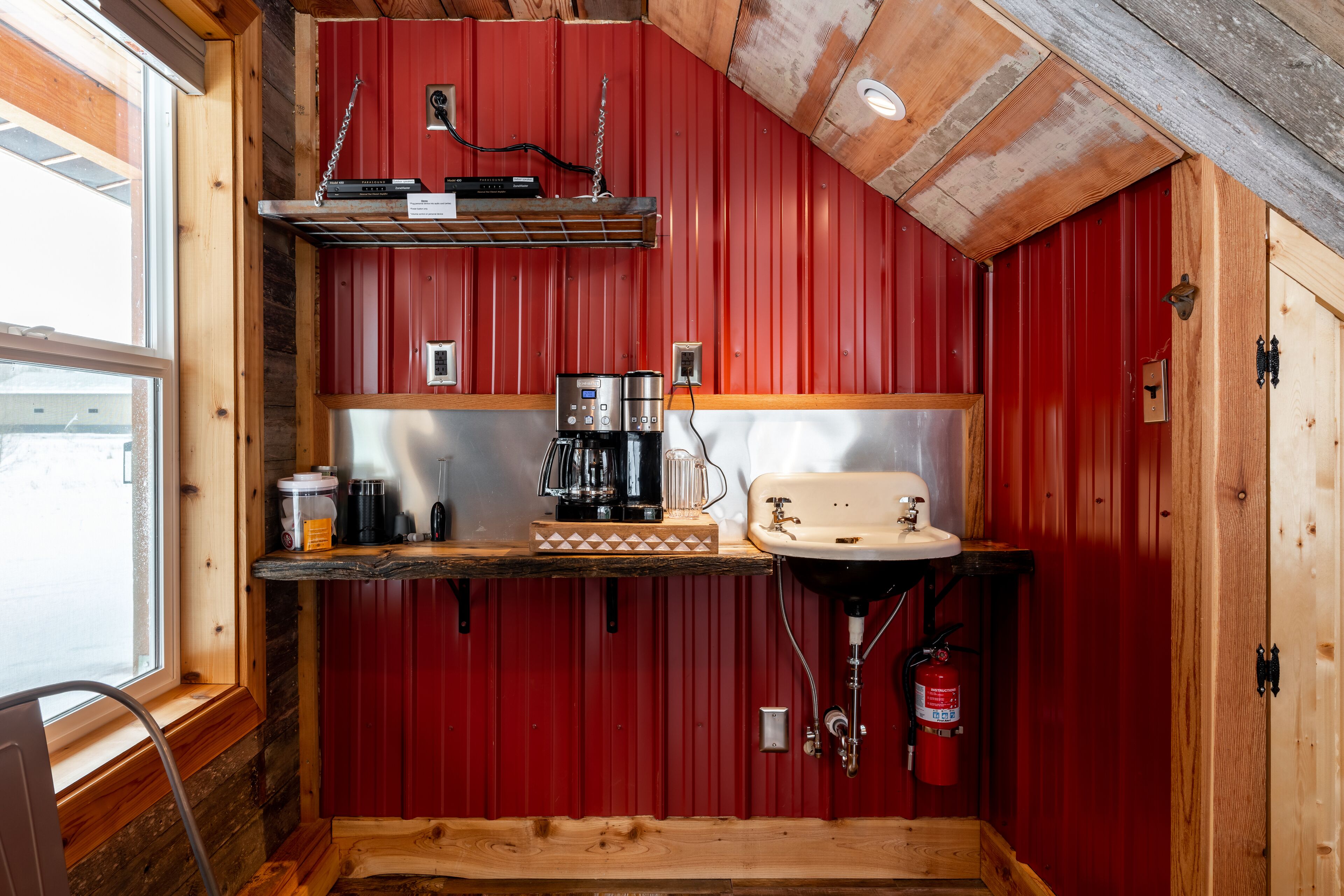 Cocina compacta con paredes rojas, encimera de madera, un lavabo, cafetera y extintor.