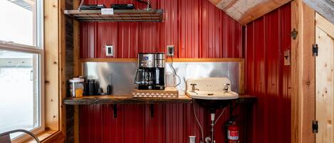 Cocina compacta con paredes rojas, encimera de madera, un lavabo, cafetera y extintor.