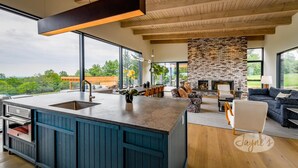 A modern kitchen with a large island, a stone fireplace, and a view of the outdoors. - Lovely 5bdrm 3bath modern home in Creemore! (Creemore)
