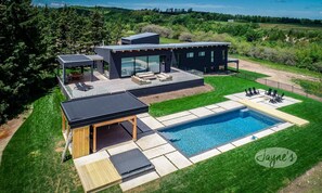 A modern house with a swimming pool, outdoor seating, and a large deck area.