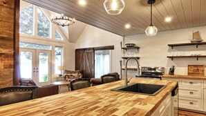 A kitchen with a wooden island, a sink, and a stove. There are chairs and a table in the dining area. - 9 bdrm, 5 bath, Lake Rosseau, Private! Guest Cottage and Cabin! Sand Beach! (Port Carling)