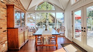 A dining area with a large table and chairs, a wooden cabinet, and large windows offering a view of the outdoors. - 9 bdrm, 5 bath, Lake Rosseau, Private! Guest Cottage and Cabin! Sand Beach! (Port Carling)