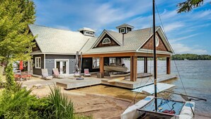 A lakeside cabin with a covered dock, outdoor seating, and a boat. - 9 bdrm, 5 bath, Lake Rosseau, Private! Guest Cottage and Cabin! Sand Beach! (Port Carling)