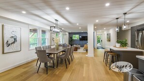 Una cocina moderna con electrodomésticos de acero inoxidable, un comedor con mesa y sillas de madera, y una sala de estar con sofá y televisor.