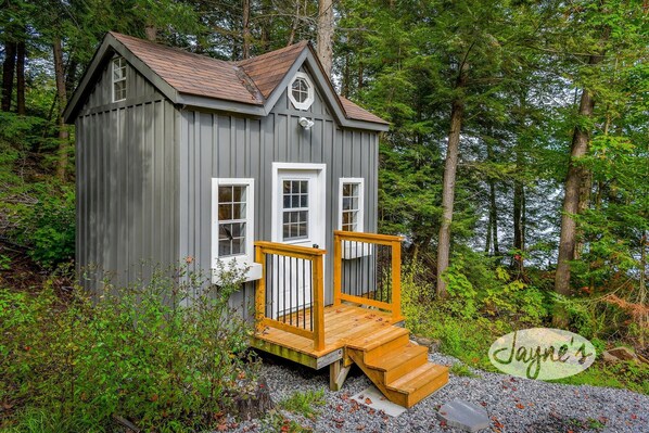 A small wooden cabin with a porch, surrounded by dense forest.