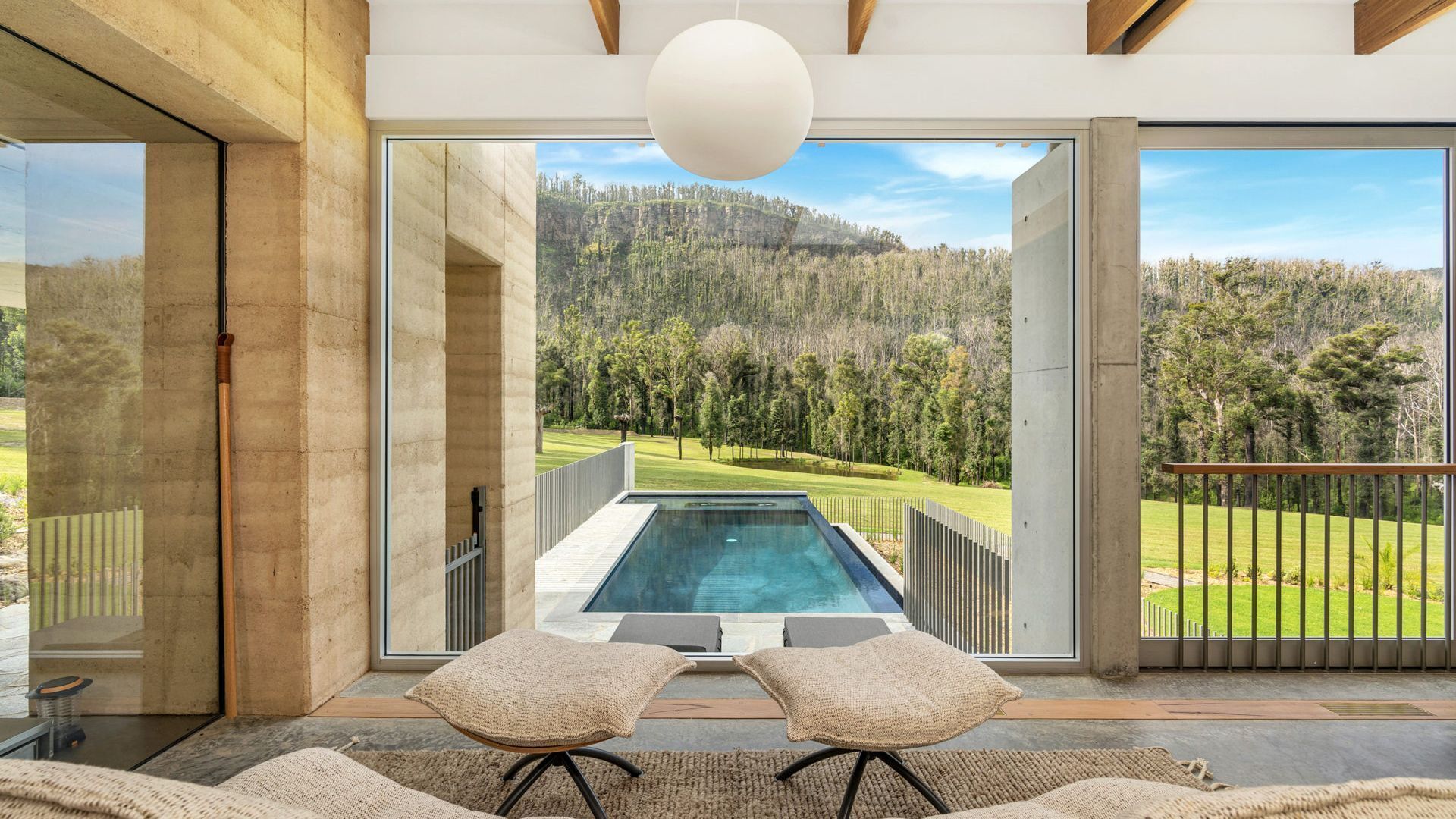 Ein modernes Interieur mit einer großen Glasdoor, die zu einem Pool und einer Aussicht auf eine bewaldete Landschaft führt.