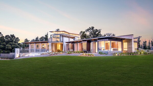 Une maison moderne à deux étages, dotée de grandes fenêtres, de fondations en pierre et d’une pelouse bien entretenue.