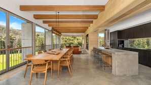 A modern kitchen with a large island, a dining area with wooden tables and chairs, and large windows offering a view of the outdoors. - Robinson's Run - The ultimate luxury country retreat (Kangaroo Valley)