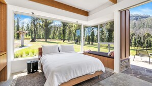 A bedroom with a large bed, a bench by the window, and a view of a forested area. - Robinson's Run - The ultimate luxury country retreat (Kangaroo Valley)