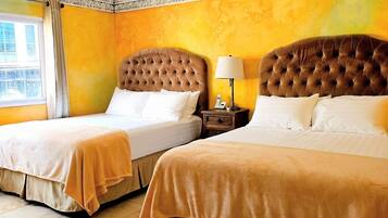 A hotel room with two beds, a window with curtains, a bedside table with a lamp, and an air conditioning unit.
