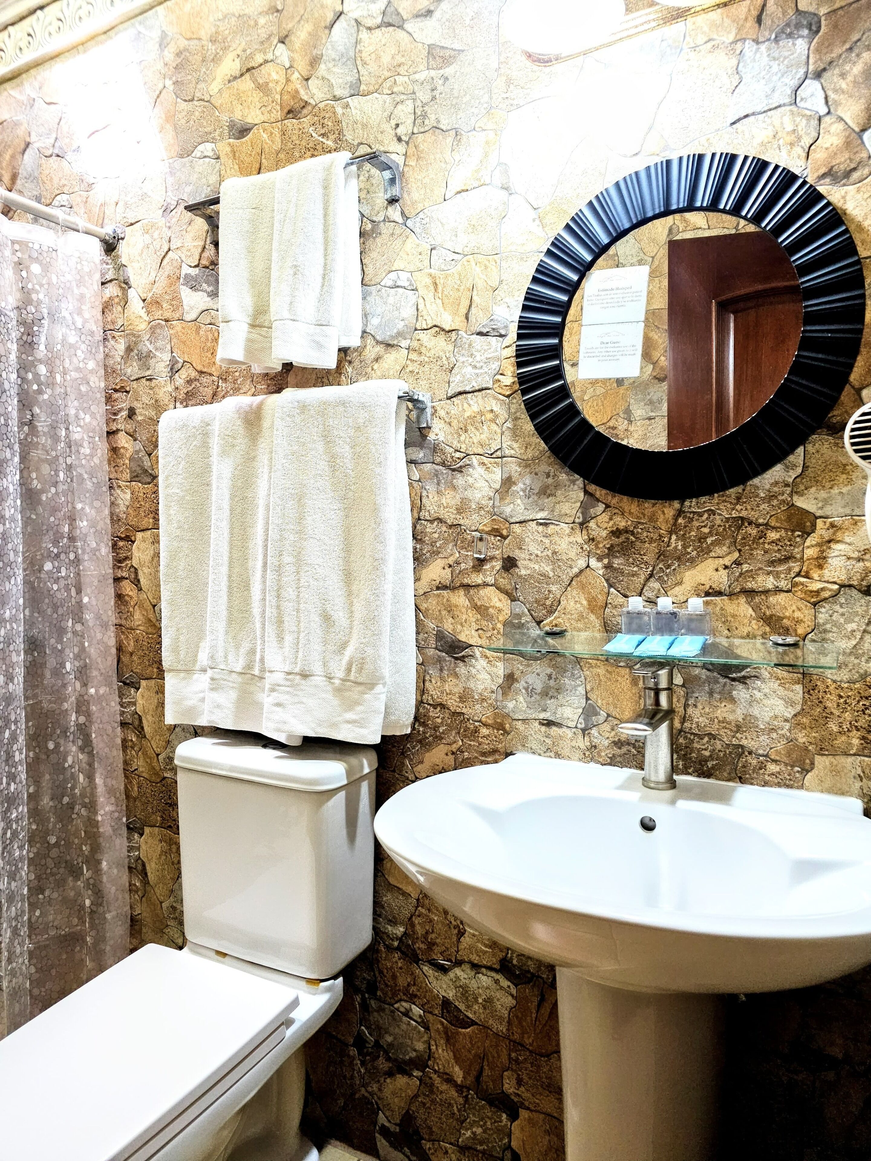 A bathroom with a stone wall, a toilet, a sink, and a mirror.
