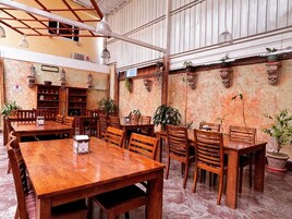 A spacious dining area with wooden tables and chairs, potted plants, and a rustic wall with shelves.
