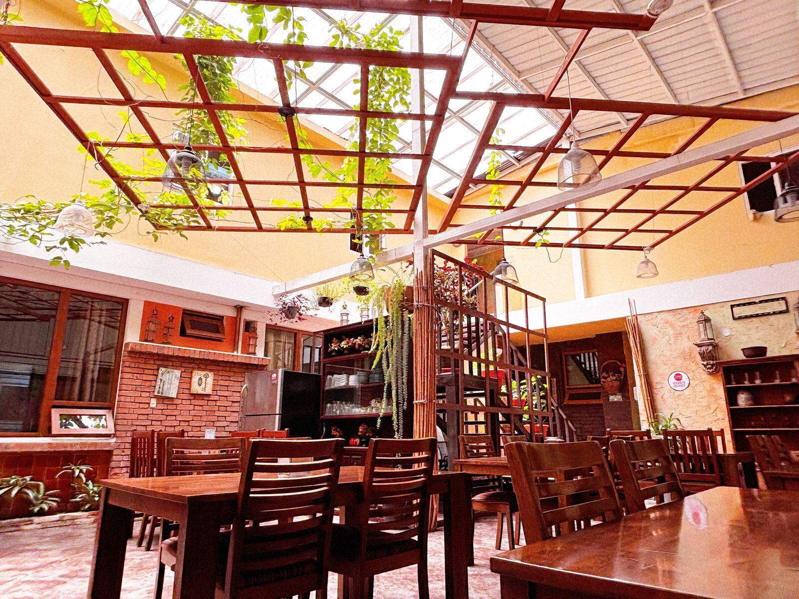 Un comedor interior con mesas y sillas de madera, una pared de ladrillo con cuadros enmarcados y un techo con diseño de cuadrícula.