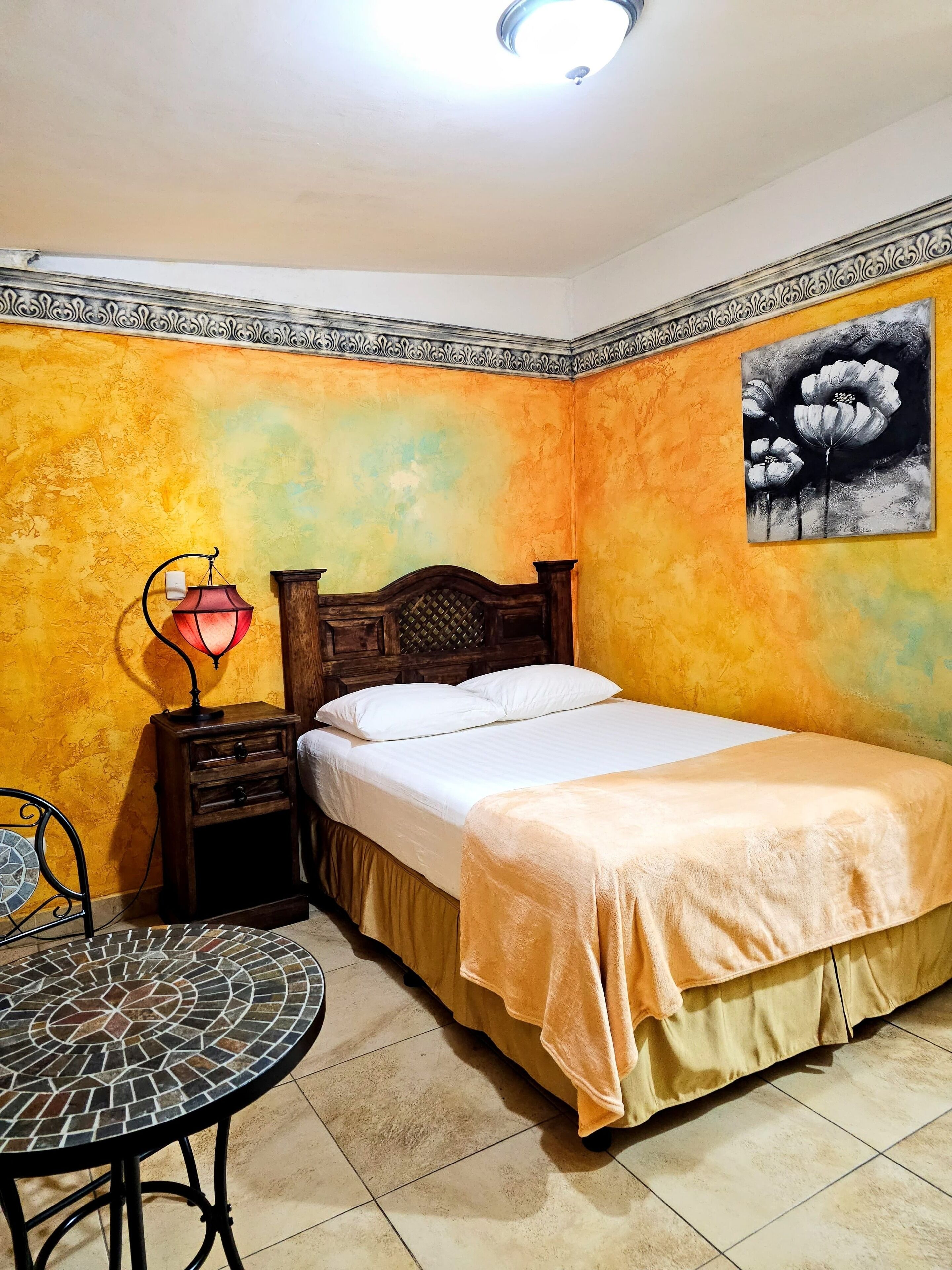 Ein Schlafzimmer mit Bett, Nachttisch, Lampe und einem Wandbild.