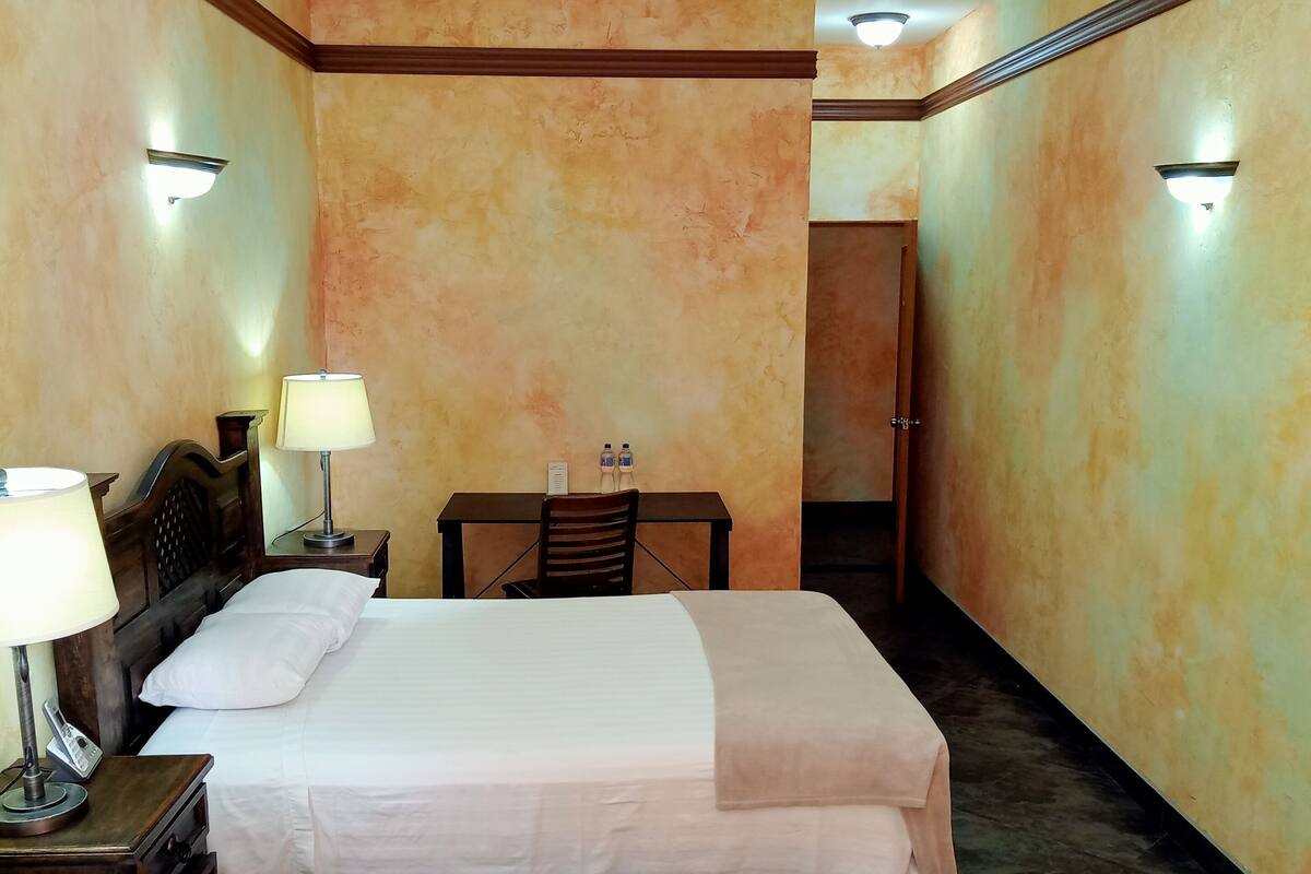 A hotel room with two beds, a desk, a chair, a lamp, a phone, and two water bottles on the wall.