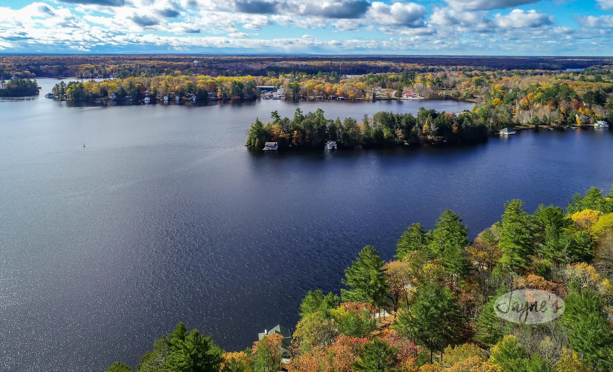 A lake surrounded by autumn-colored trees and a few buildings.