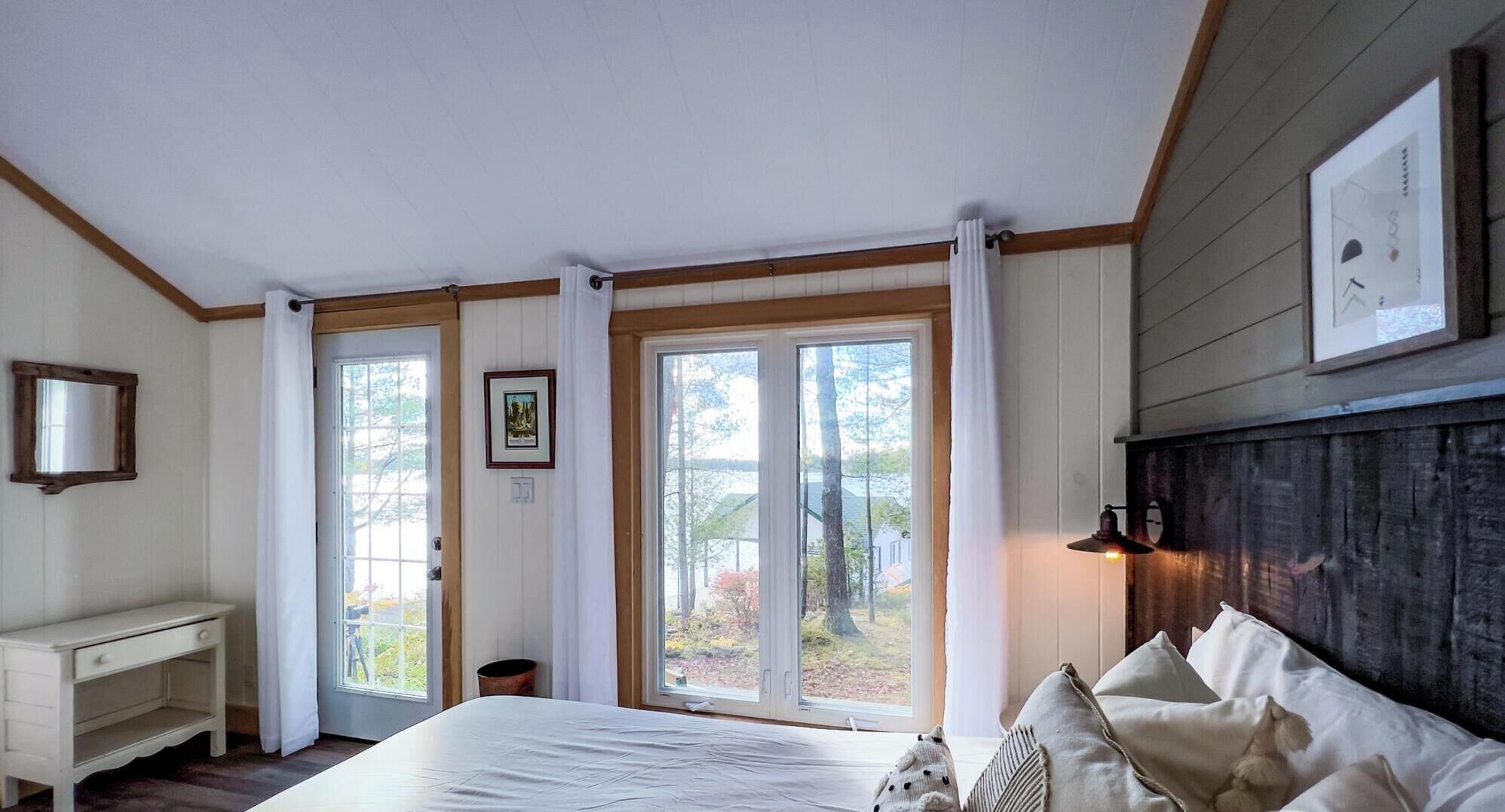 A bedroom with a large bed, a nightstand, a dresser, and a window with a view of trees and a building.