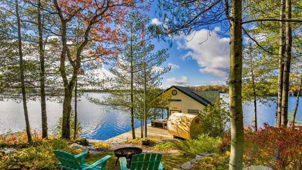 Una cabaña junto al lago con un muelle, dos sillas Adirondack y una fogata.