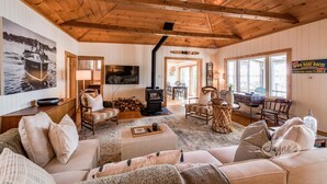 Un interior de cabaña acogedor con techo de madera, chimenea, televisor y comedor.
