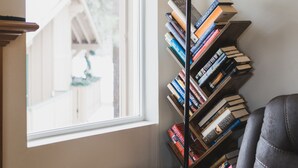 A corner of a room with a bookshelf, a chair, and a window with a view of a building outside.