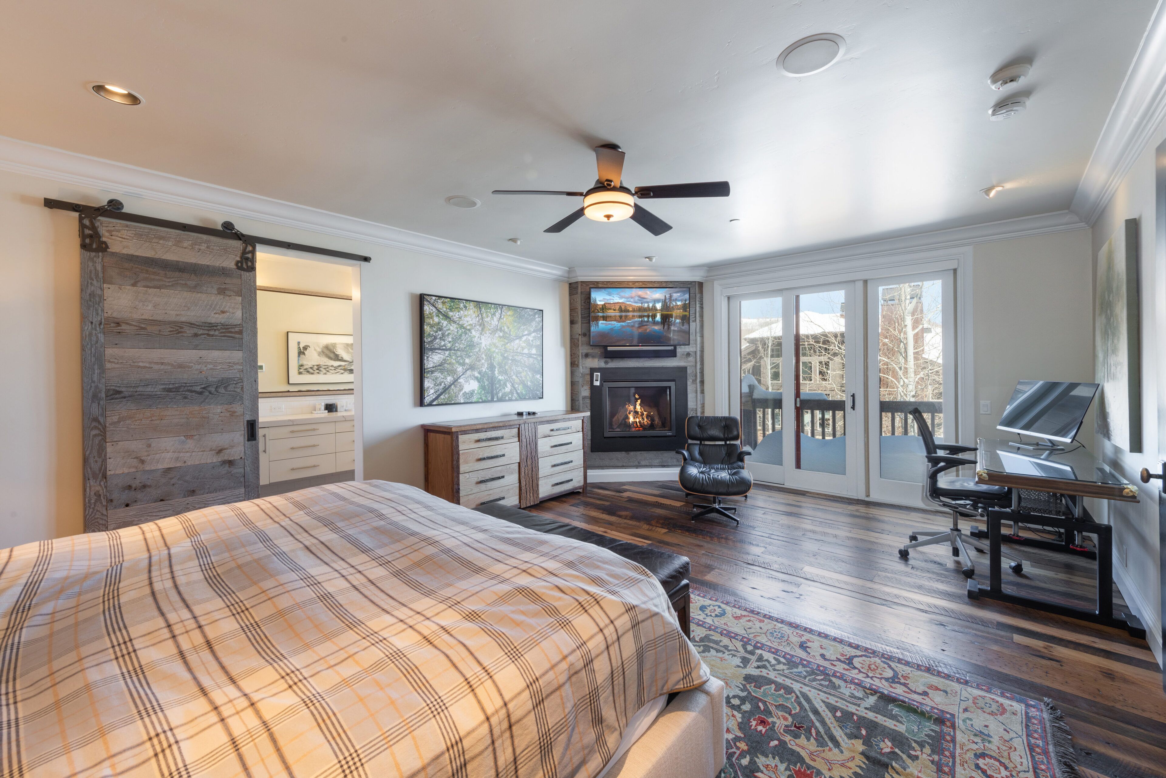 A bedroom with a bed, a fireplace, a desk, and a large window.