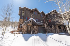 A large, multi-story stone building with a stone facade and red-framed windows, surrounded by snow and leafless trees. - Ironwood by Luxury Mountain Destinations (Park City)