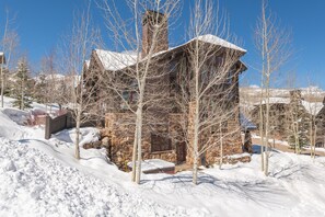 A stone cabin with a chimney, surrounded by snow-covered ground and leafless trees. - Ironwood by Luxury Mountain Destinations (Park City)