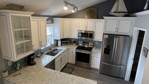 A modern kitchen with white cabinetry, stainless steel appliances, and a granite countertop. - Pelican Landing / Beach Bird Properties - Inside Oceanside Village (Surfside Beach)