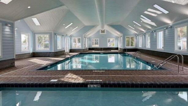 A large indoor swimming pool with a tiled deck, clear ceiling, and windows. - Pelican Landing / Beach Bird Properties - Inside Oceanside Village (Surfside Beach)