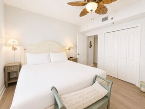 Une chambre à coucher avec un lit, des tables de chevet, un ventilateur de plafond et une porte.