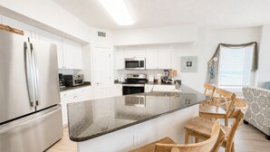 A modern kitchen with white cabinets, stainless steel appliances, a granite countertop, and wooden chairs.