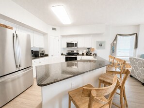 A modern kitchen with white cabinets, stainless steel appliances, a granite countertop, and wooden chairs.