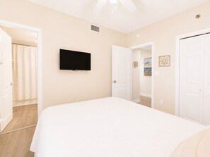Ein Schlafzimmer mit Bett, Fernseher, einer Tür und Blick auf einen anderen Raum.